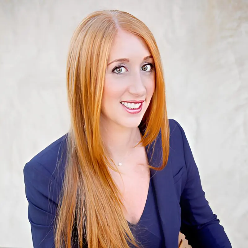 A woman with long red hair wearing a blue jacket.